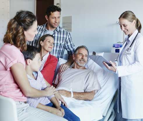 Mann liegt auf einem Krankenhausbett uns ist umgeben von seiner Familie