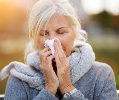 Eine Frau mit Schnupfen säubert sich die Nase