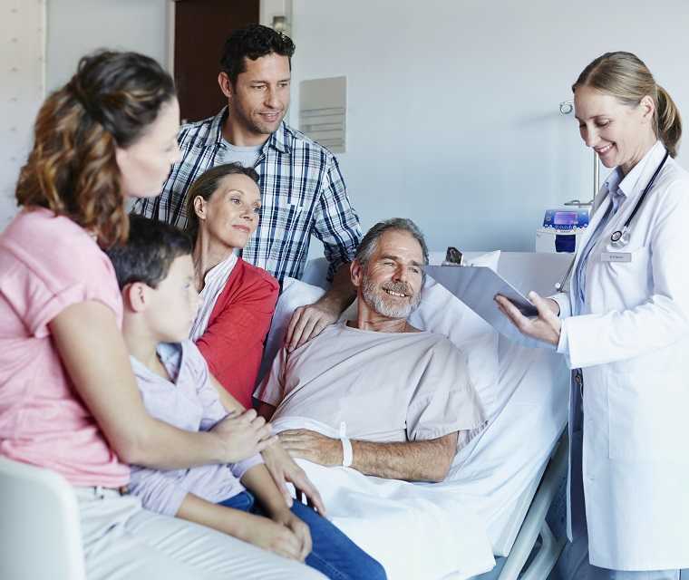 Mann liegt auf einem Krankenhausbett uns ist umgeben von seiner Familie