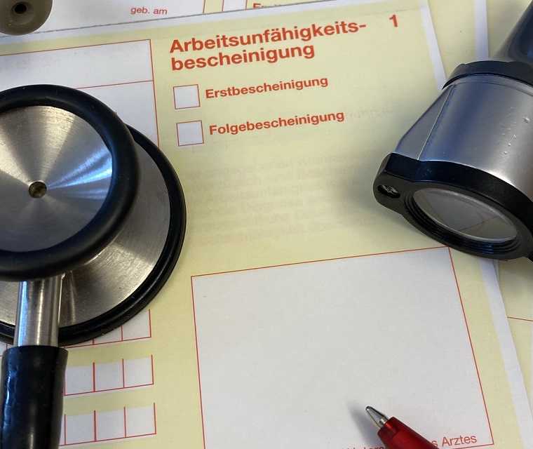 Auf dem Tisch eines Arztes liegt die Arbeitsunfähigkeitsbescheinigung für einen Patienten