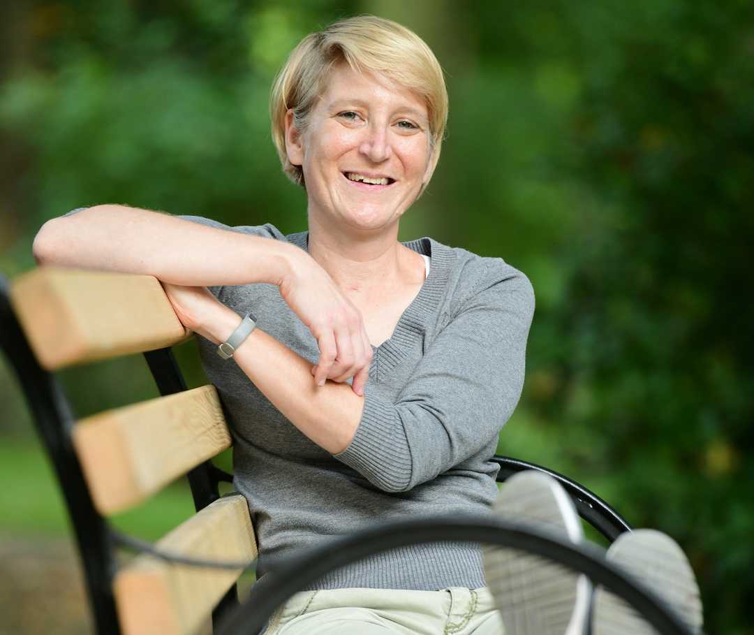 Patientin Franziska sitzt auf einer Parkbank und lacht in die Kamera